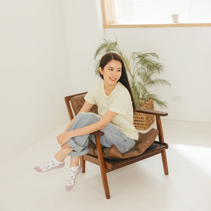 Woman sitting on a chair wearing a light yellow shirt and ankle compression socks with floral designs.