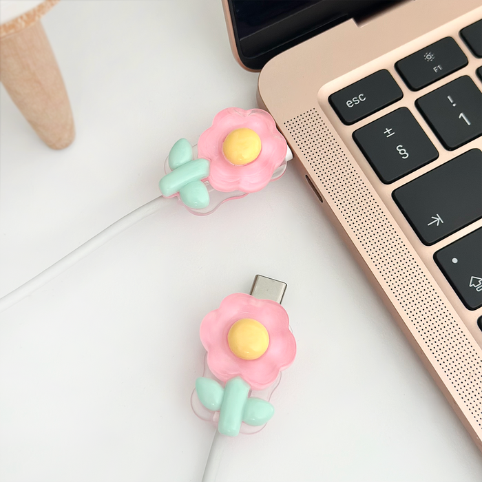 Flower-shaped cable cover charm decorates USB-C cables plugged into a rose gold laptop on a white surface.
