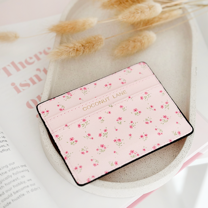 Pink card holder with ditsy floral pattern on a light tray, beige dried flowers softly blurred in the background.