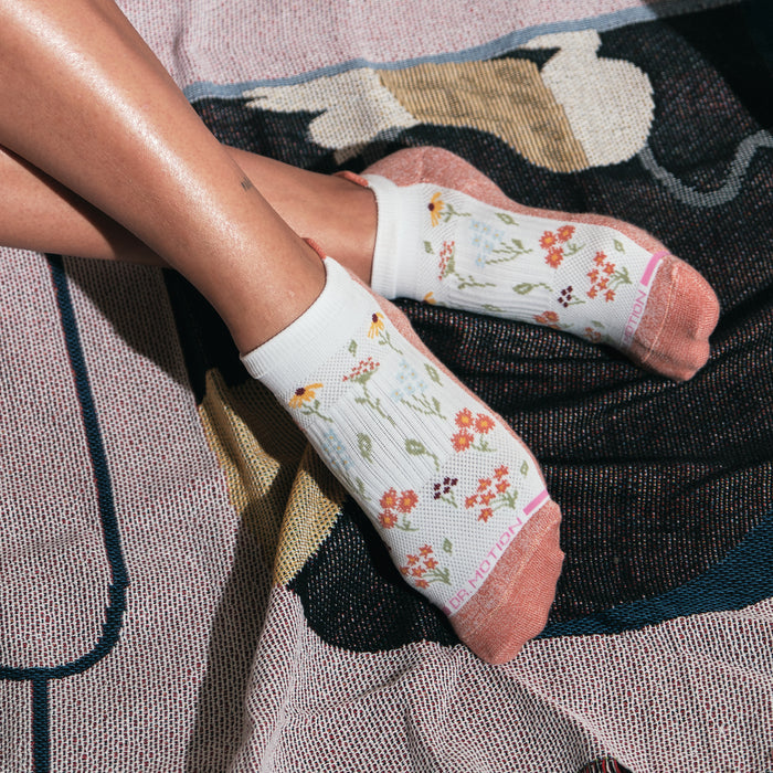 Ankle compression socks with a floral pattern and pink accents, resting on a textured surface.