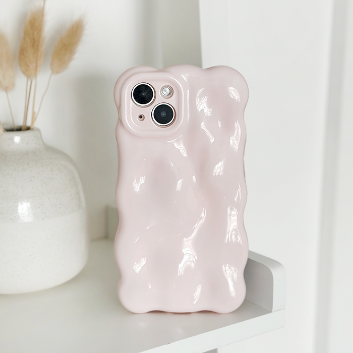 Powder pink 3D bubble phone case upright on a white shelf next to a white vase with dried grass.