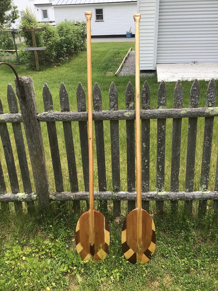 Two oars made out of four ounce fiberglass cloth fabric, wood and resin resting along a picket fence.