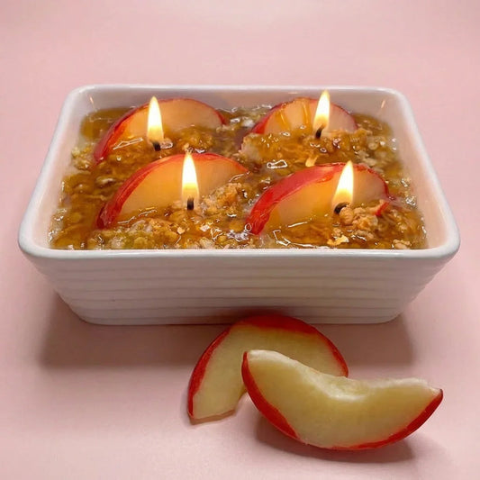 Gourmand dessert-inspired candle with apple slice toppers in a white dish, lit on pink background