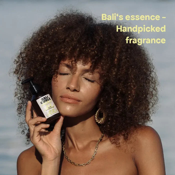 Woman with curly hair holding Bali Curls defining gel, showcasing natural curls and handpicked fragrance