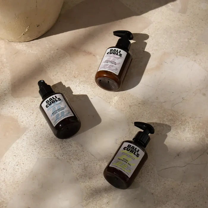 Bali Curls curly hair products: hydrating cream, defining gel, and refreshing spray on marble