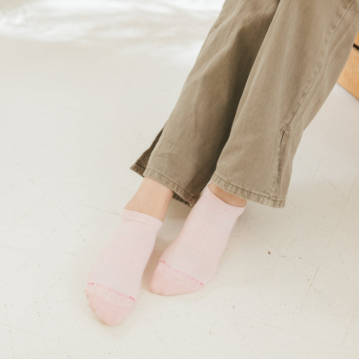 Light pink ankle compression socks worn with olive green pants, resting on a white floor.