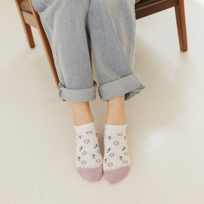 Ankle compression socks with a floral and bee pattern, worn with rolled-up jeans.