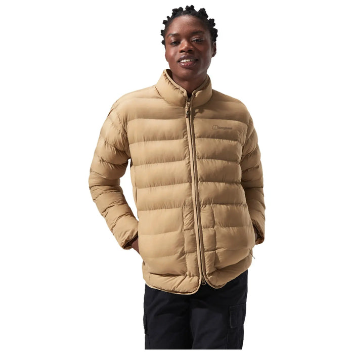 A person is standing and smiling while wearing a tan puffer jacket with a high collar, showcasing a casual and warm style in a neutral background.
