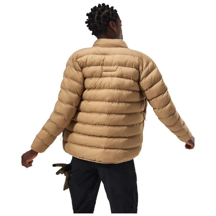 A person wearing a tan puffer jacket is turning away with an outstretched arm in a neutral setting emphasizing the jacket's texture and style.