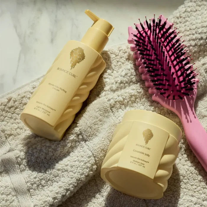 Bounce Curl styling cream and ceramide jelly with pink detangling brush on towel