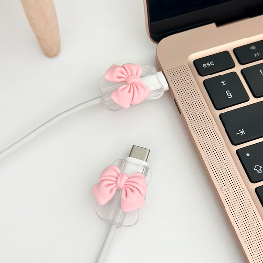 Pink bow cable cover charm from Coconut Lane on a rose gold laptop, clipped around a white USB-C cable.