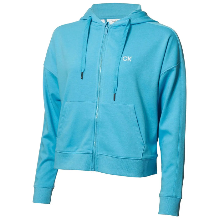 A light blue zip-up hoodie features a front pocket and drawstrings on the hood showcasing the Calvin Klein logo in white on the chest in a neutral background.