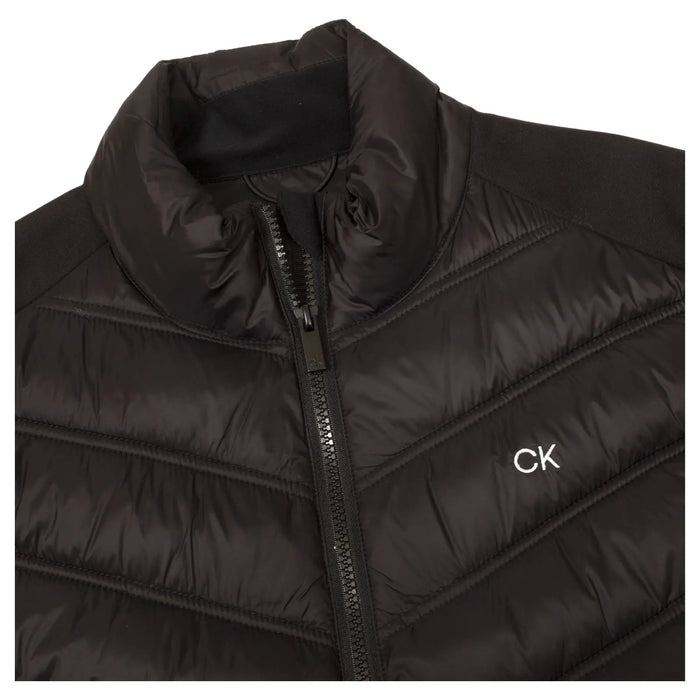 A black puffer jacket is laid flat displaying a high collar and a zippered front. The fabric has a quilted texture with a small logo embroidered on the chest.