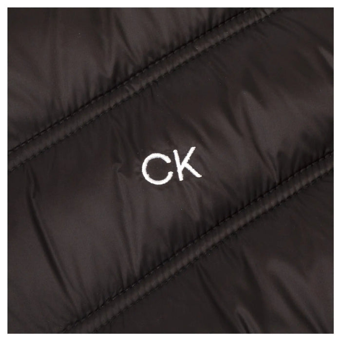 A black puffer jacket is vertically textured with a white "CK" logo prominently displayed on the fabric emphasizing its branding in a close-up view.