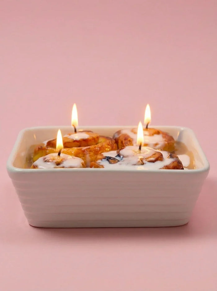 Dessert-inspired candle shaped like cinnamon rolls with icing in a white dish on pink background