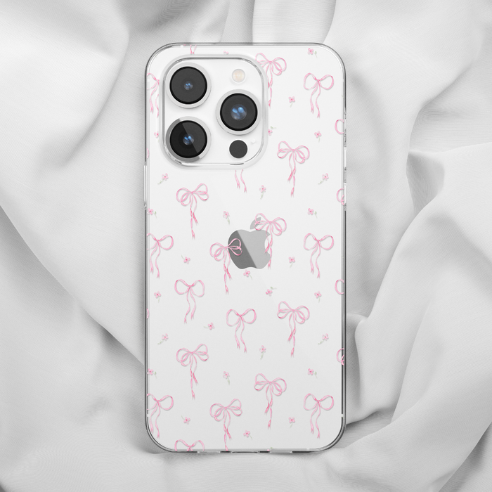 White iPhone with Coconut Lane clear phone case featuring a dainty bows pattern, placed on soft white fabric.