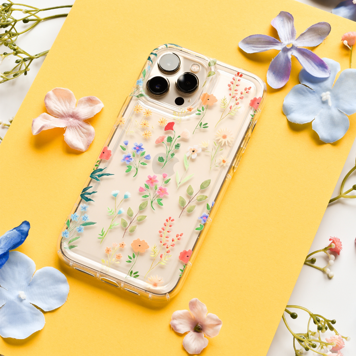 Clear phone case with a colourful wildflower pattern on a yellow surface, surrounded by pastel flower petals.