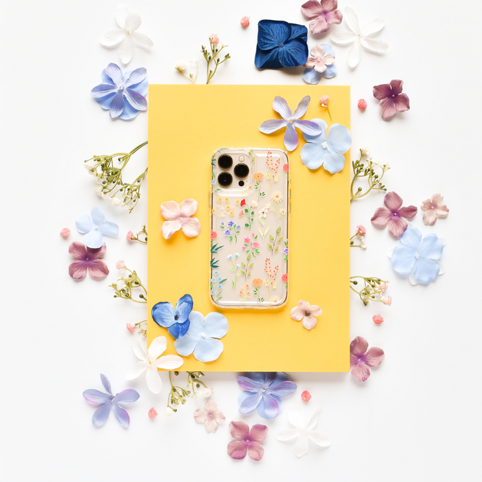 Clear phone case with colourful pastel wildflower pattern, displayed on a yellow surface.