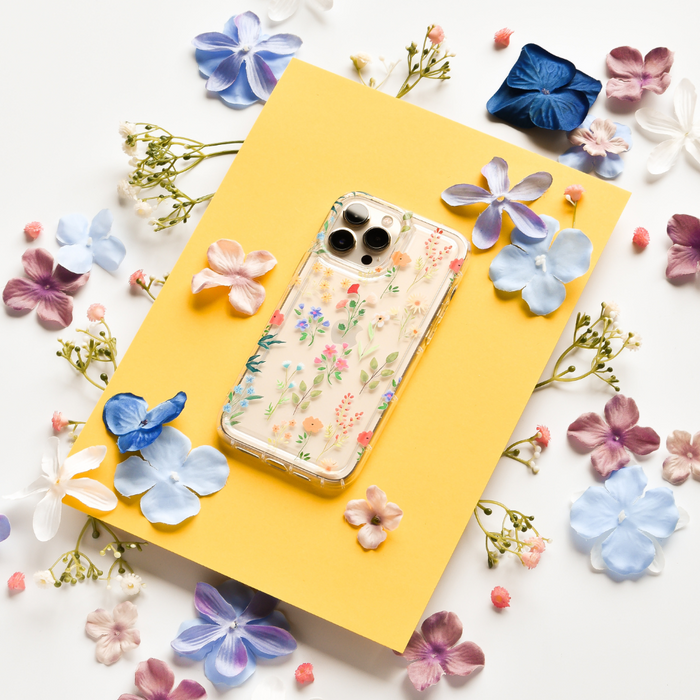 Clear phone case with colorful wildflower pattern on yellow paper, surrounded by bright artificial flowers.