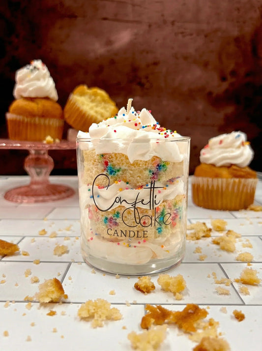 Confetti cake candle in a glass jar with whipped topping and colorful sprinkles, surrounded by cupcakes.