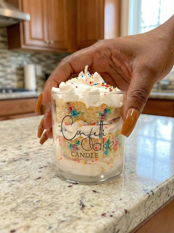 Hand holding a confetti cake candle with colorful sprinkles, whipped topping, on kitchen counter.