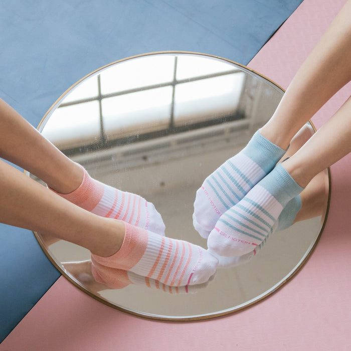 Ankle compression socks in pink and blue stripes reflected in a round mirror on a colorful surface.