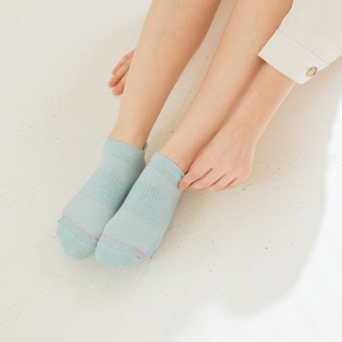 Light blue ankle compression socks with contrasting stripes, worn by a person sitting on a white floor.