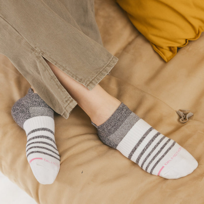 Ankle compression socks with a contrast stripe design, worn with cropped pants on a neutral surface.