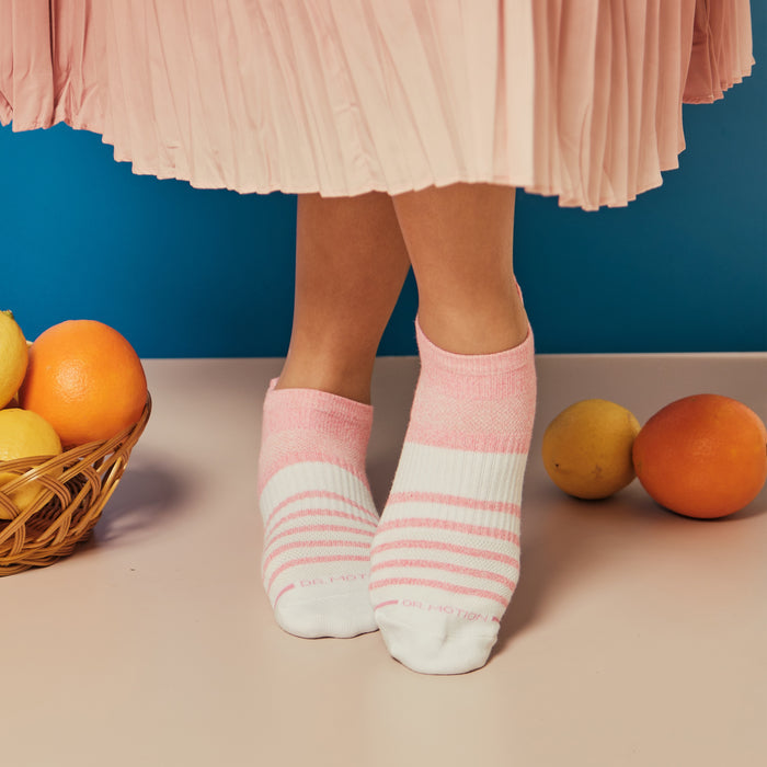 Ankle compression socks with pink and white stripes, worn by a person standing near a basket of fruit.