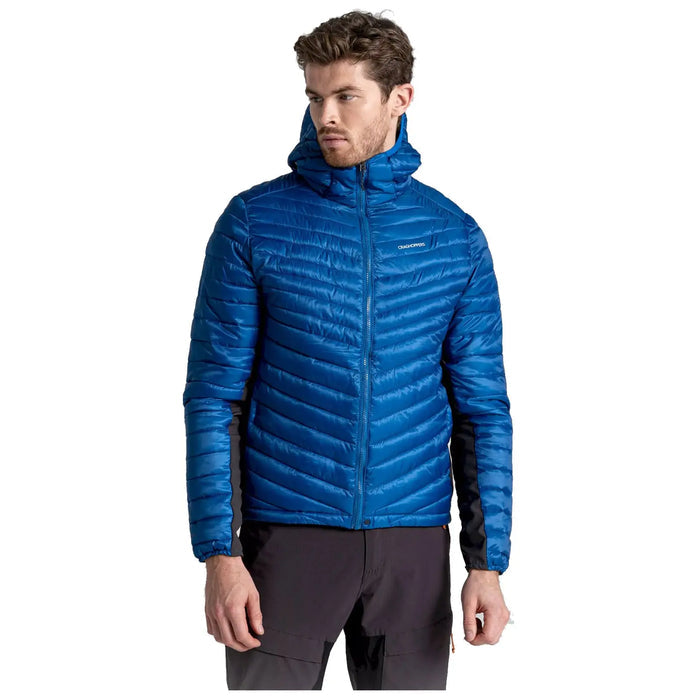 A man is wearing a bright blue puffy jacket with a hood standing upright and looking slightly to the side in a neutral setting with no visible background elements.