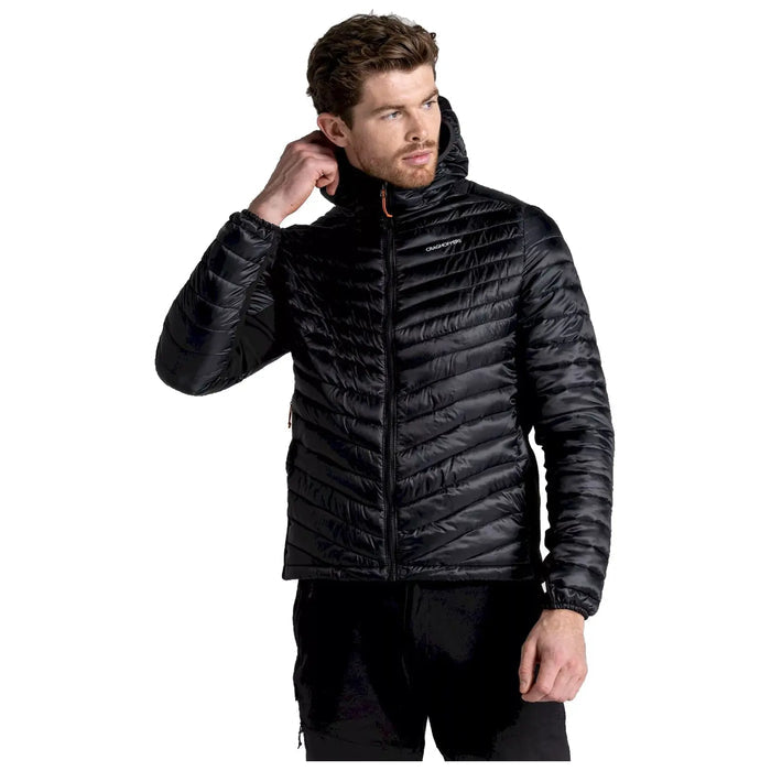 A man is adjusting the hood of a black puffer jacket with a zippered front while standing in a neutral background, showcasing a stylish and functional outerwear piece.