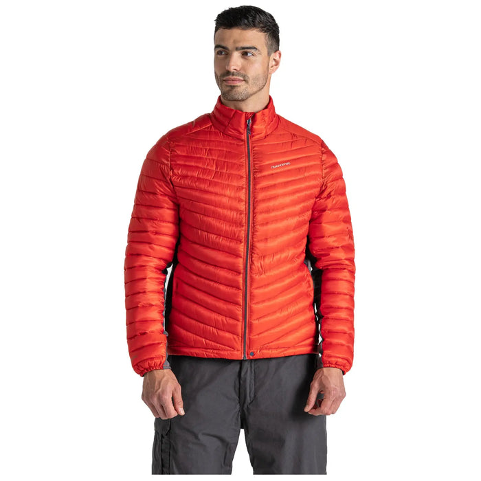 A man dressed in a bright red puffy jacket stands facing slightly to the side with a neutral expression while wearing gray pants and holding his hands in front of him.