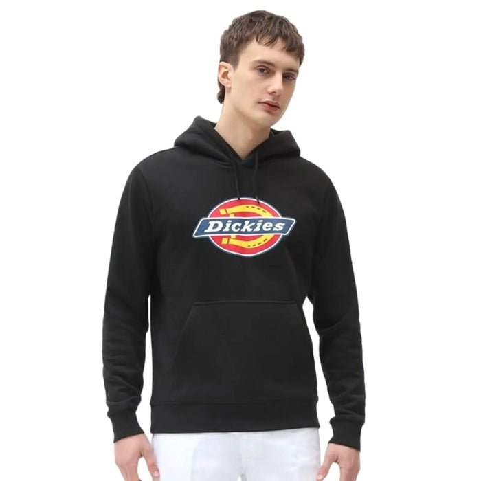 A young man wears a black hoodie with a colorful logo. He stands confidently with his hands slightly visible in front of him, against a plain white background.