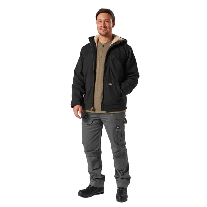 A man stands confidently wearing a black hooded jacket and gray cargo pants with pockets. He appears to be in a neutral setting with a light background.