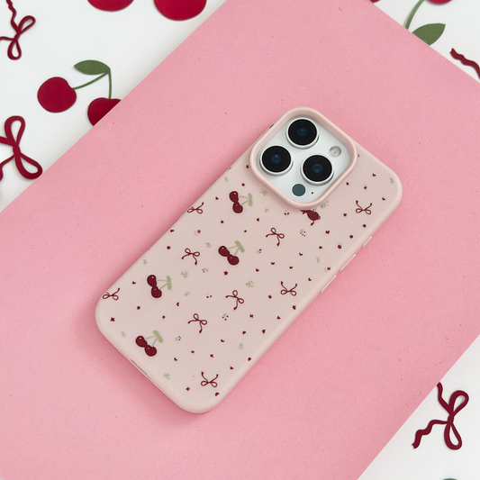 Pink Coconut Lane phone case with bows and cherry pattern on a pink surface, surrounded by cherry illustrations.