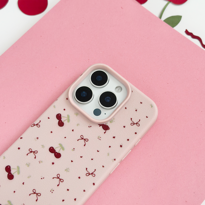 Pink phone case with bows and cherries pattern on a pink surface, set against a pink and red background.