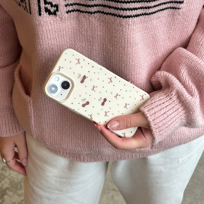 Soft white phone case with bows and cherries pattern, held by a person wearing a pink sweater.