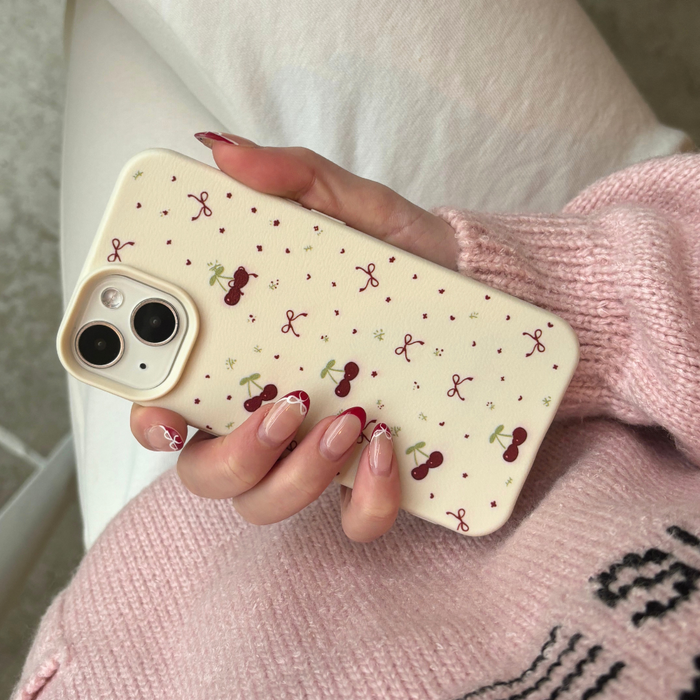 Soft white phone case with small bows and cherries pattern, held by a hand with painted nails.