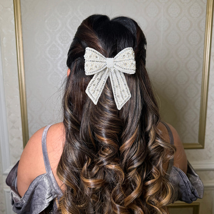 A silver-colored embellished crystal and pearl hair bow clip worn on a woman's hair.