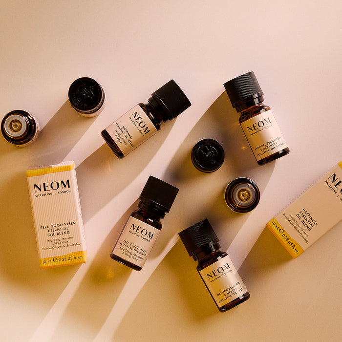 Assorted NEOM essential oil blend bottles and caps arranged on a light background with product boxes, showing multiple mood-boosting scents.
