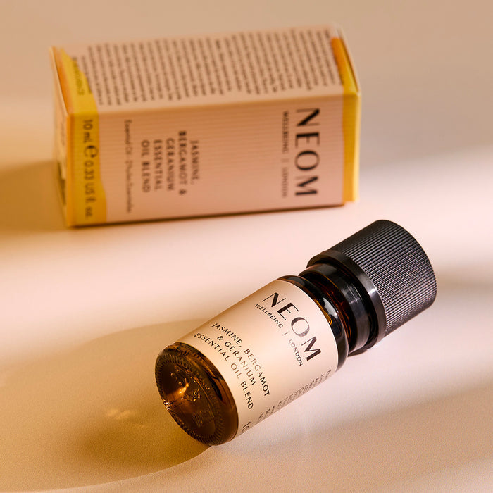 NEOM Jasmine, Bergamot & Geranium essential oil blend bottle lying on a surface with its product box behind it.