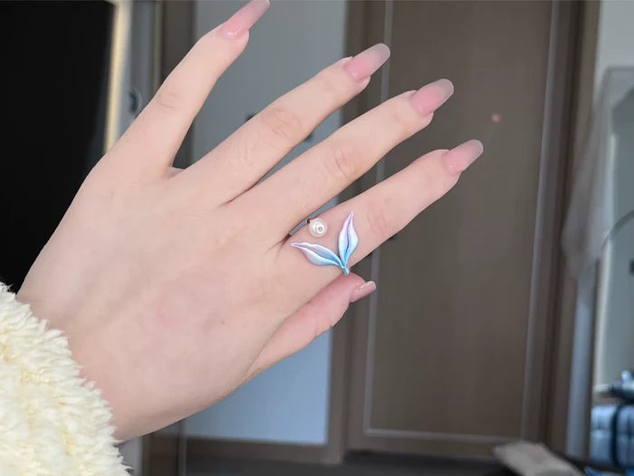 A hand wearing a blue mermaid tail ring and holding a blue mermaid tail necklace-2