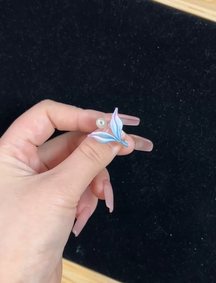 A hand wearing a blue mermaid tail ring and holding a blue mermaid tail necklace-3