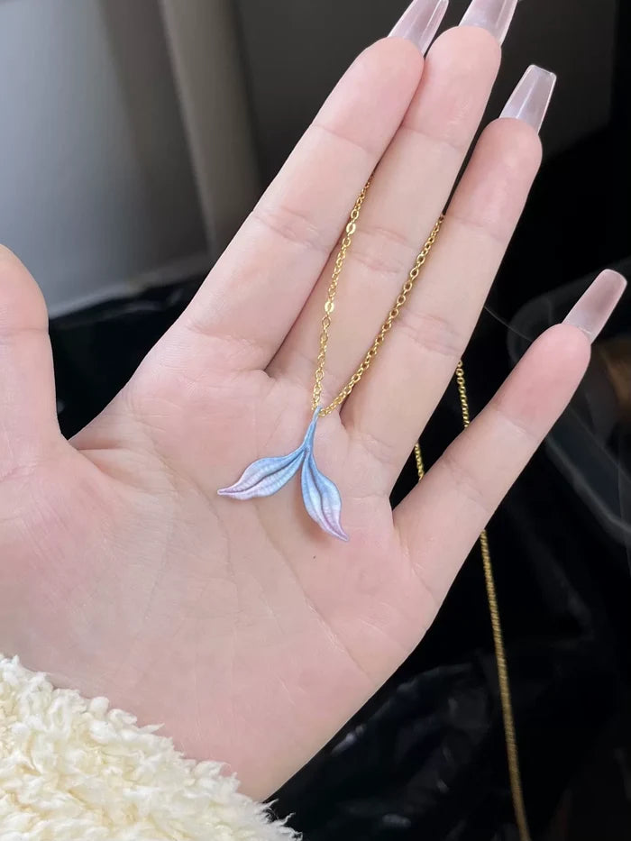 A hand wearing a blue mermaid tail ring and holding a blue mermaid tail necklace-4