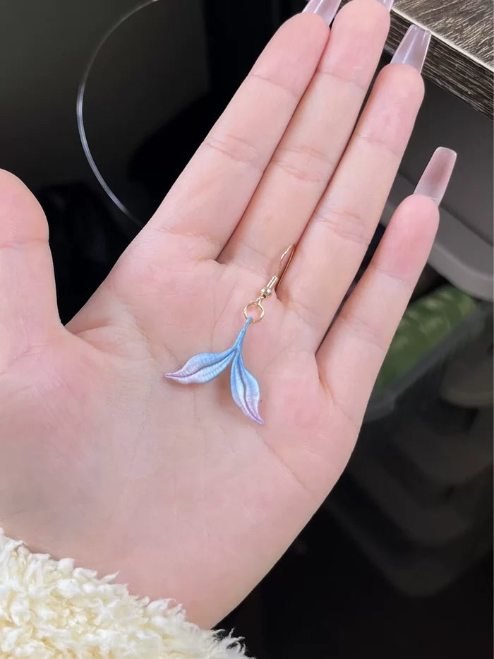 A hand wearing a blue mermaid tail ring and holding a blue mermaid tail necklace-5