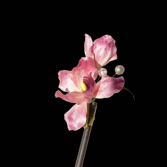 Handcrafted Ronghua Pink Iris hairpin featuring soft velvet-textured silk petals and delicate pearl accents on a wooden base.
