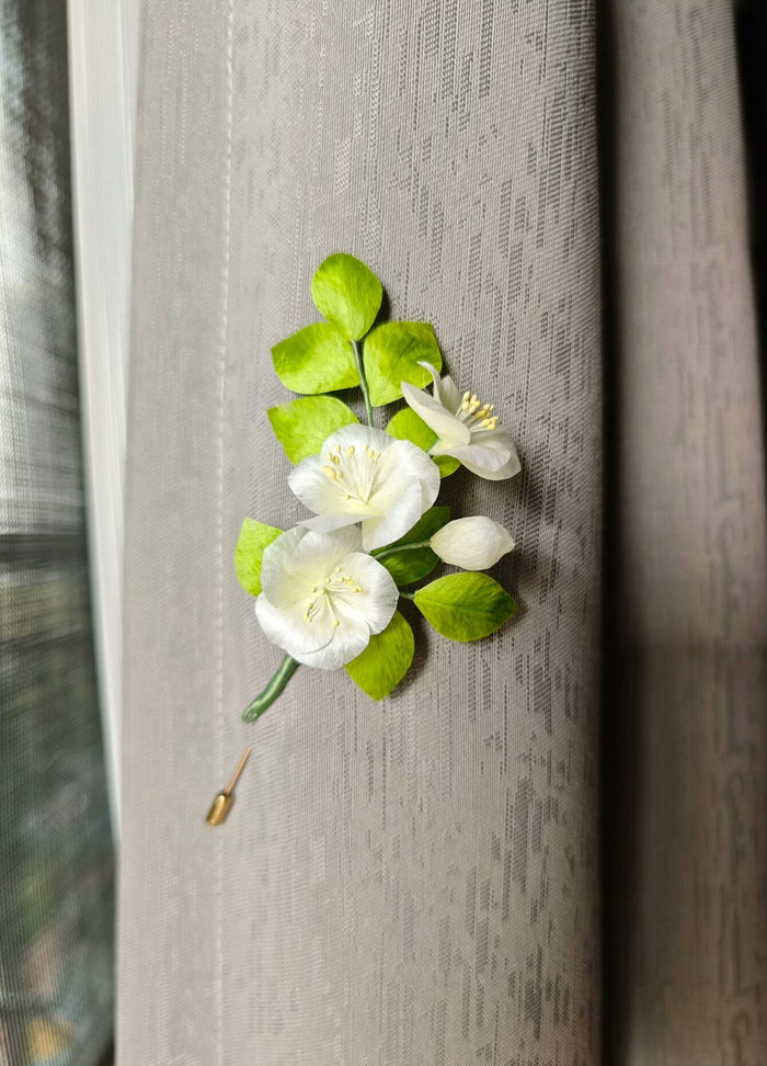 A handmade Ronghua pear flower small white flower brooch with green leaves and white flowers attached to a curtain.