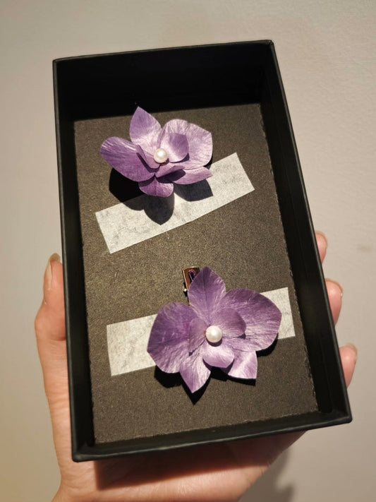 Handheld black box containing two purple Ronghua phalaenopsis hair accessories/brooches with pearl centers