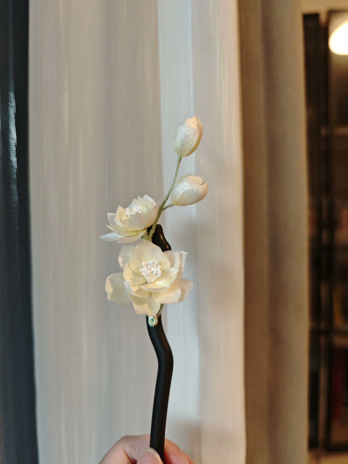 Handmade Ronghua white jasmine hairpin with lifelike flowers held against a light - colored background