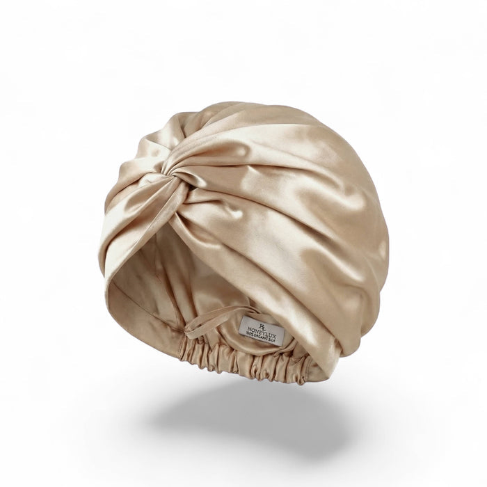 A champagne gold silk hair cap with an elasticized gathered bottom, shown floating on a white background with a soft shadow underneath.